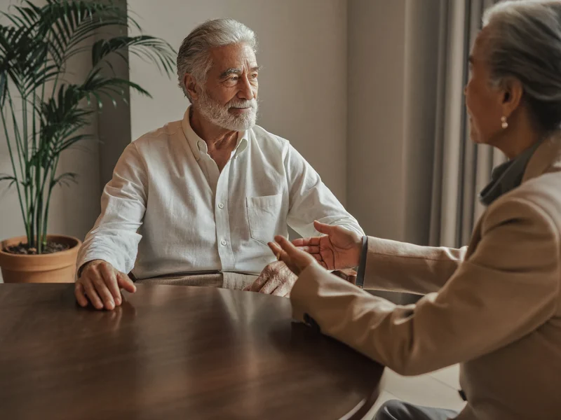 Un uomo anziano ascolta con attenzione la consulente durante un colloquio