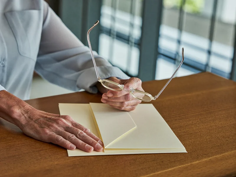Mani anziane con occhiali da lettura su cartellina e buste